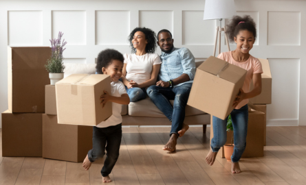 Couple smiling on sofa with kids running and holding moving boxes