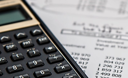Calculator sitting on top of paper with money calculations
