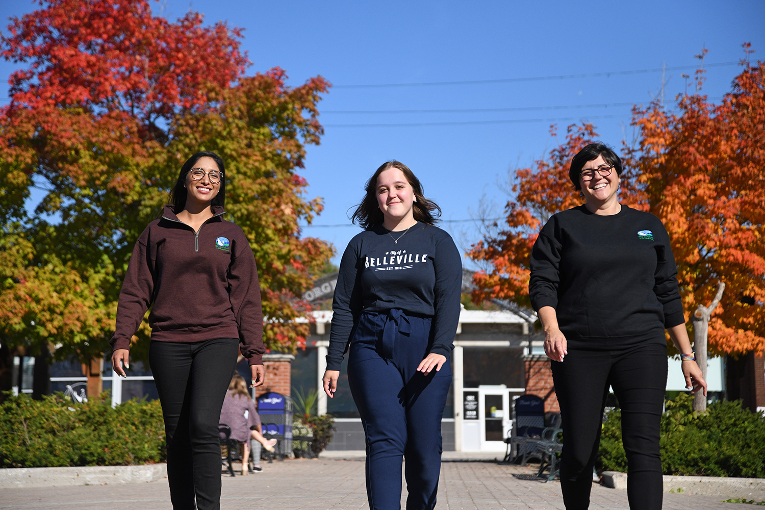 Photo of 3 people waering City of Belleville Merch walking with fall trees in the background.